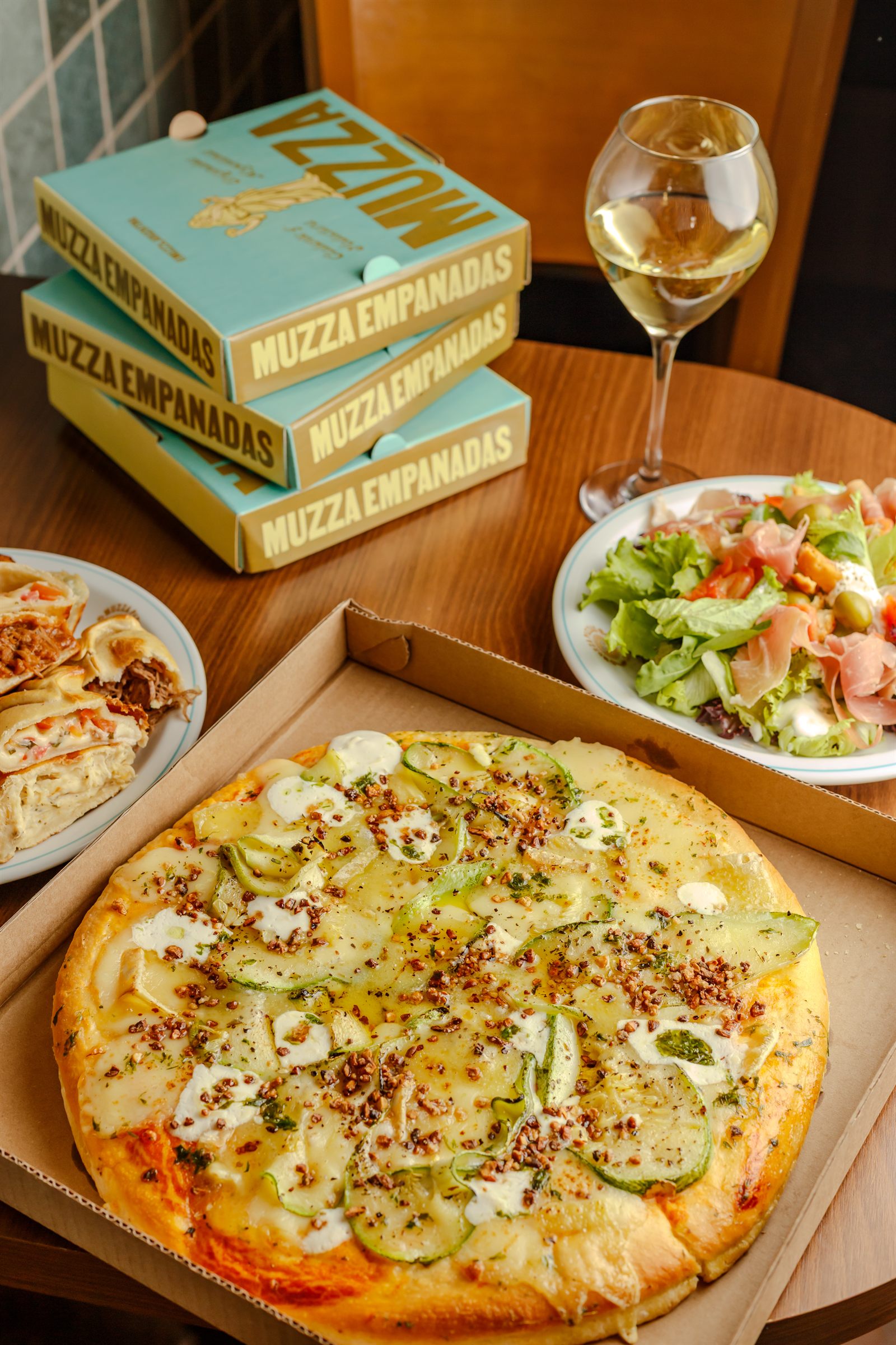 Mesa Muzza completa — pizza, empanadas, vinho